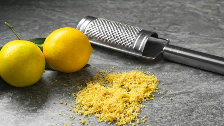 Lemon zest on marble surface with microplane grater and two lemons