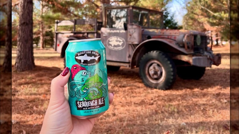 A can of Dogfish Head SeaQuench Ale in front of a rustic truck in a wooded area