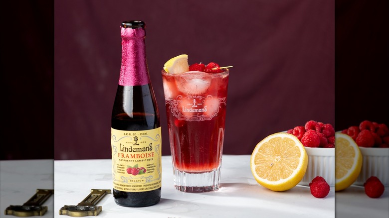 A bottle of Lindemans Framboise next to a poured glass with oranges and raspberries nearby