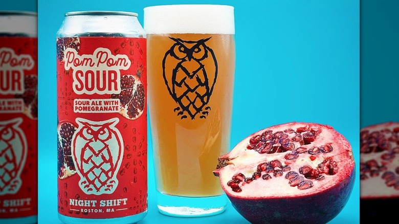 A can of Pom Pom sour ale next to a poured glass and a half pomegranate on a blue background