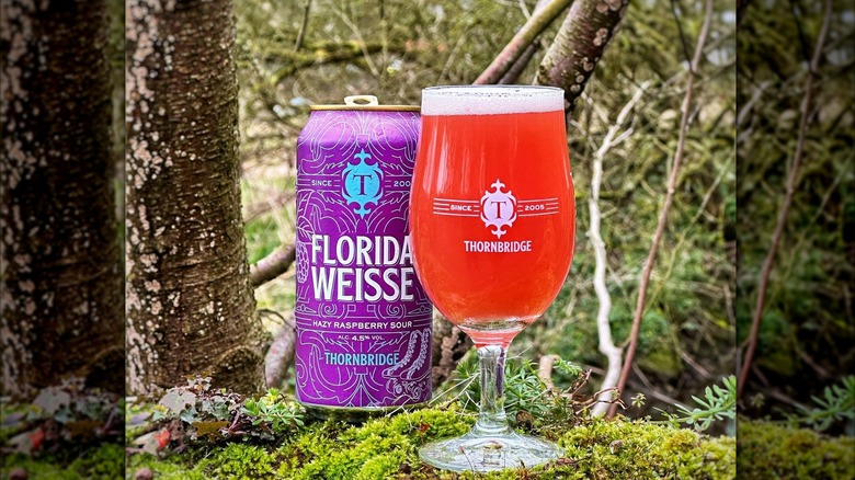 A can of Florida Weisse next to a poured glass in a wooded forest