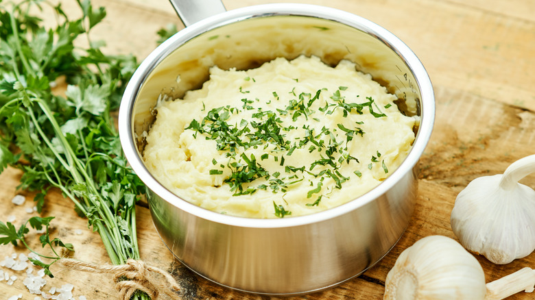 A pot of mashed potatoes with parsley and whole garlic bulbs on the side