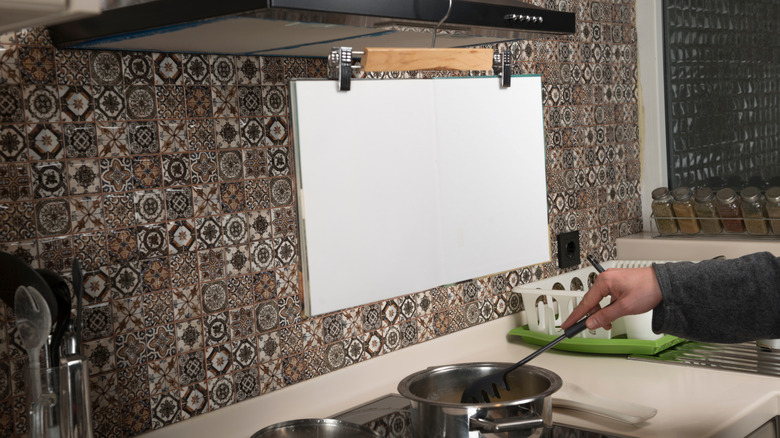 Pants hanger suspending a cookbook above the stove while a person's hand stirs a pot