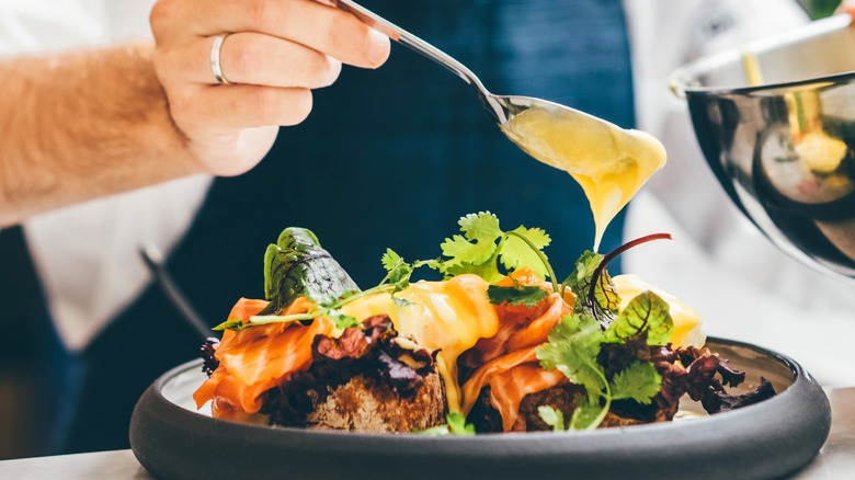 Chef spooning sauce onto vegetables and salmon