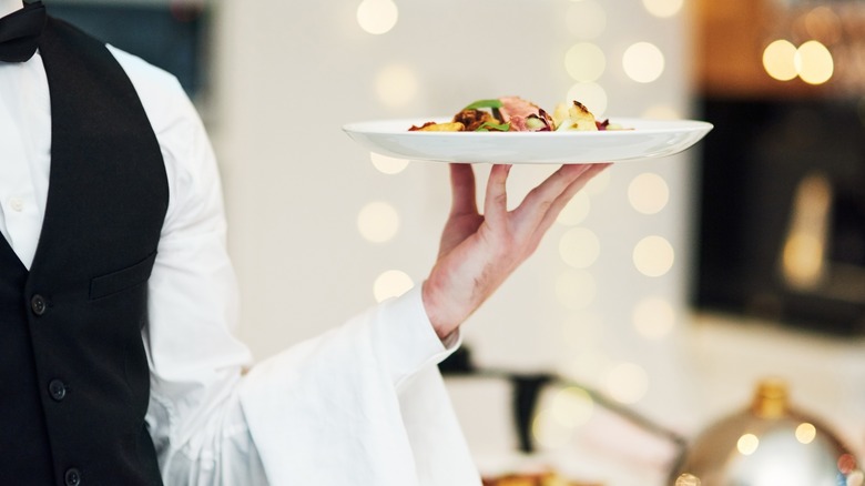 Well-dressed waiter carrying a plate of food