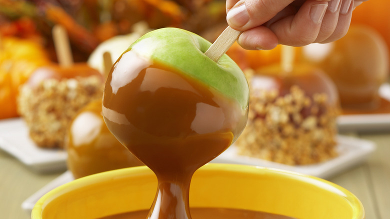 Person dipping a Granny Smith apple on a stick into caramel.