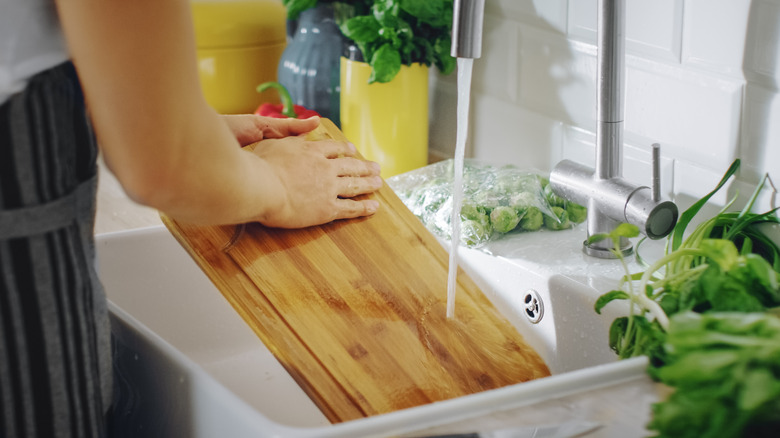 Woman washing a cutting board in kitchen sink