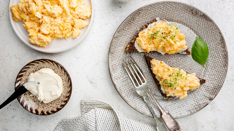 a plate of scrambled eggs, a plate of scrambled egg toast, and a small bowl with cream cheese