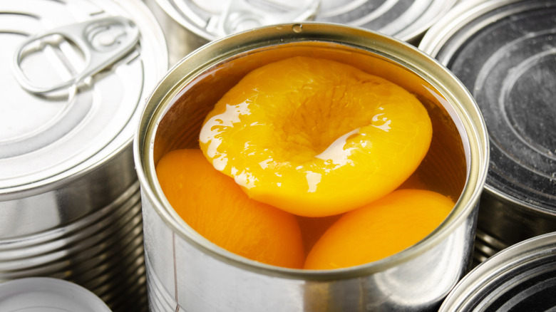 Open can of peach halves surrounded by other cans