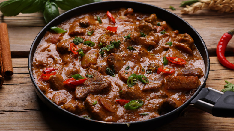 A pan of beef curry with diced hot peppers on top