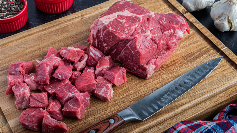 Chuck roast being cubed on a cutting board