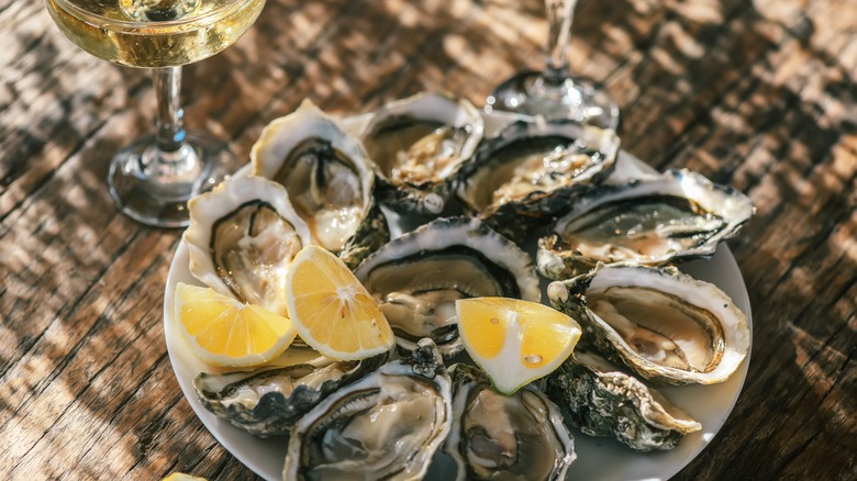 oysters in a bowl with lemon next to a glass of wine