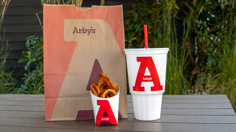 Arby's bag, curly fries, and drink on a picnic table