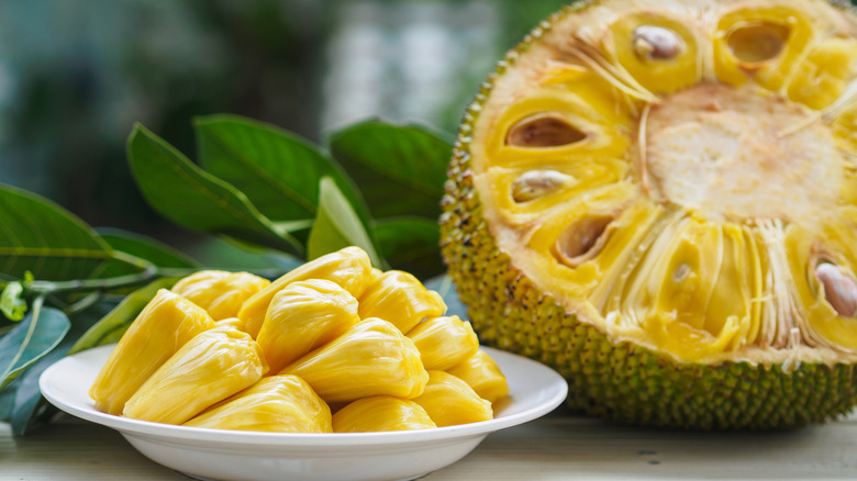 A plate of fresh jackfruit flesh next to a whole jackfruit cut in half