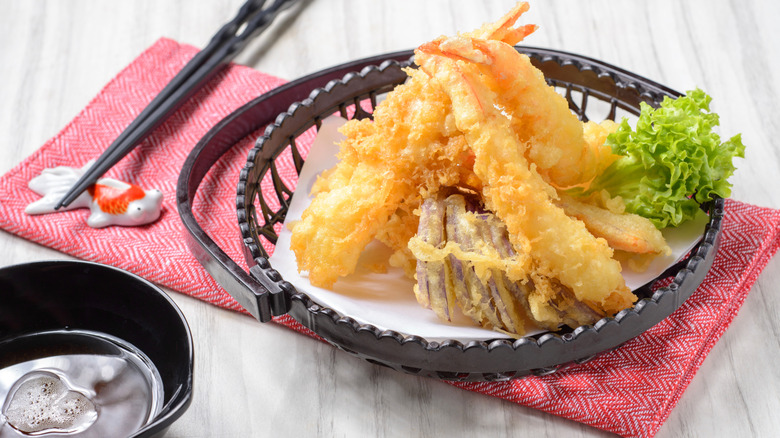 A basket of fish and shrimp tempura, with chopsticks and a bowl of soy sauce