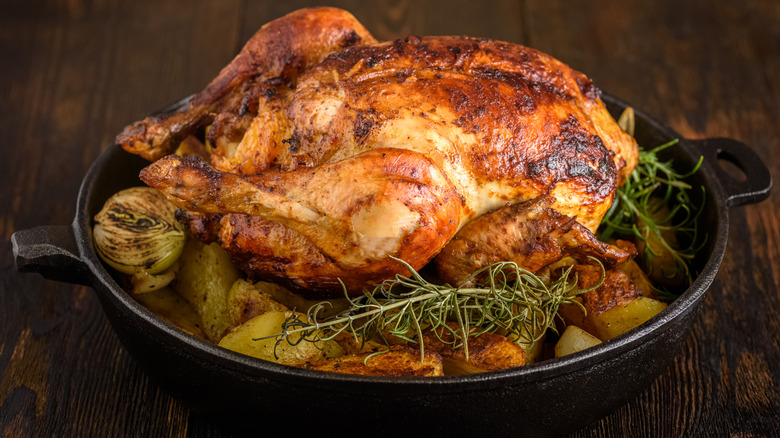 Roast chicken in cast iron pan with onions, herbs, and potatoes