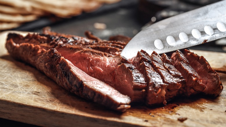 Knife cutting grilled flank steak