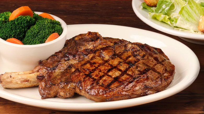 A plate with a bone-in ribeye and a bowl of broccoli and carrots from Texas Roadhouse