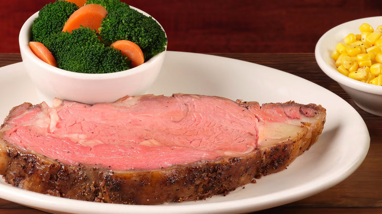 A piece of prime rib on a plate with a bowl of broccoli from Texas Roadhouse