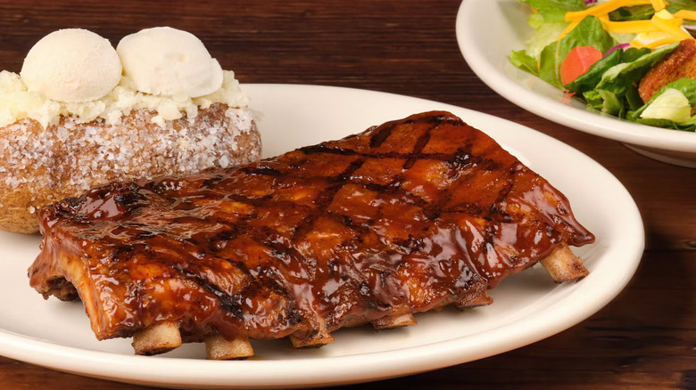 A plate of ribs with a baked potato from Texas Roadhouse