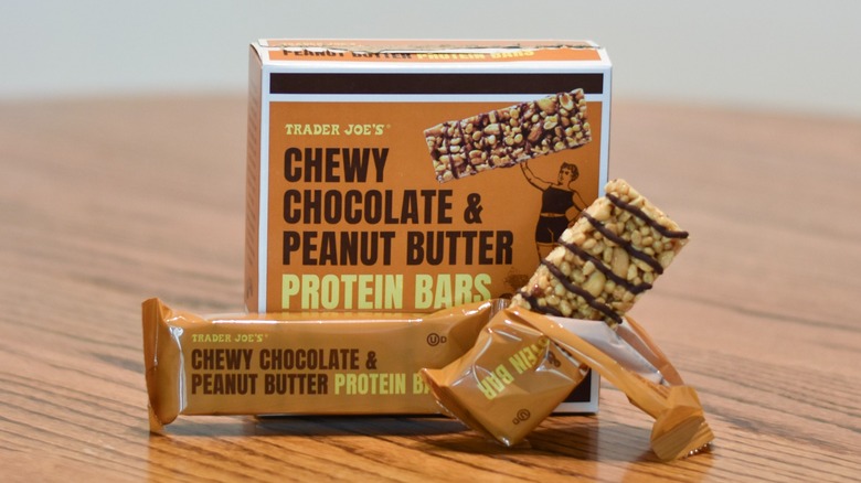 A box of Trader Joe's chewy chocolate and peanut butter protein bars sits behind an unwrapped bar on a wooden table.