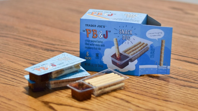 A box of Trader Joe's snacks is displayed with individual packs in front of it on a wooden table.