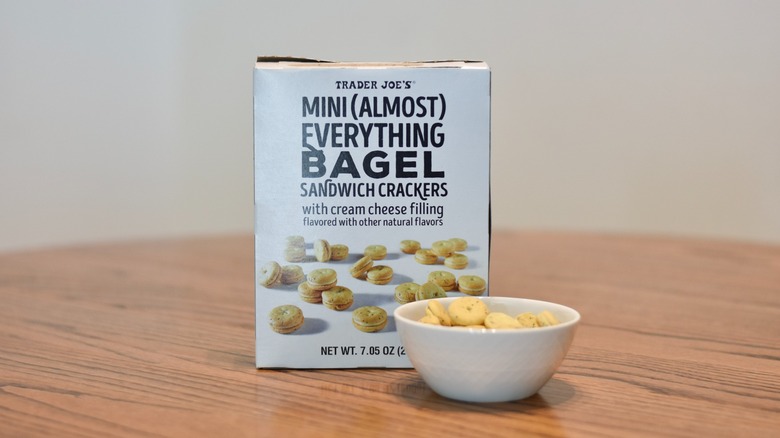 A box of Trader Joe's crackers is behind a white bowl of crackers on a wooden table.