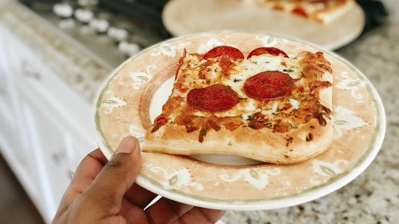 Slice of pepperoni pizza on a plate in front of a pizza stone