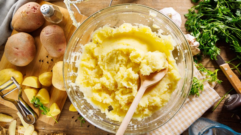 Mashed potatoes stirred in bowl with raw potatoes nearby