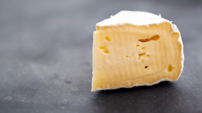 A wedge of brie cheese on a charcoal surface