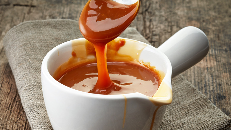 A bowl of melted caramel with a ribbon of caramel from a spoon above.