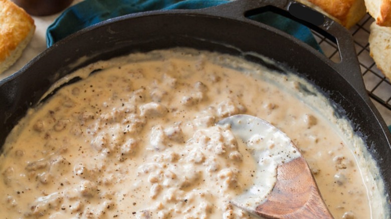 Wooden spoon stirring a cast iron pan of sausage gravy