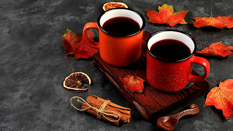 Mugs with mulled wine sit on tray surrounded by leaves and spices.