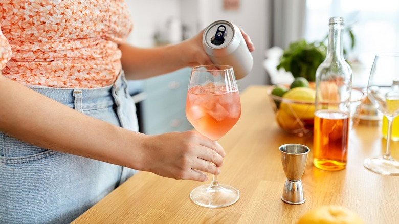 Person pouring a canned drink into a glass