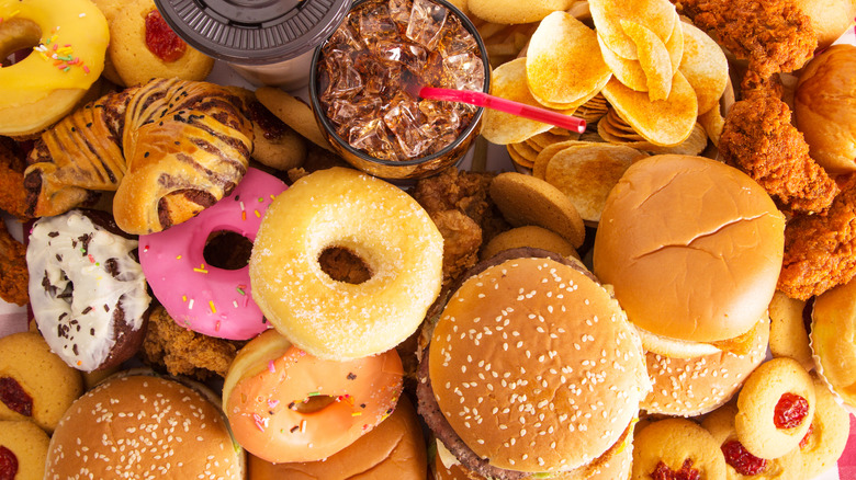 pile of burgers, donuts, chips, and cookies next to soft drink