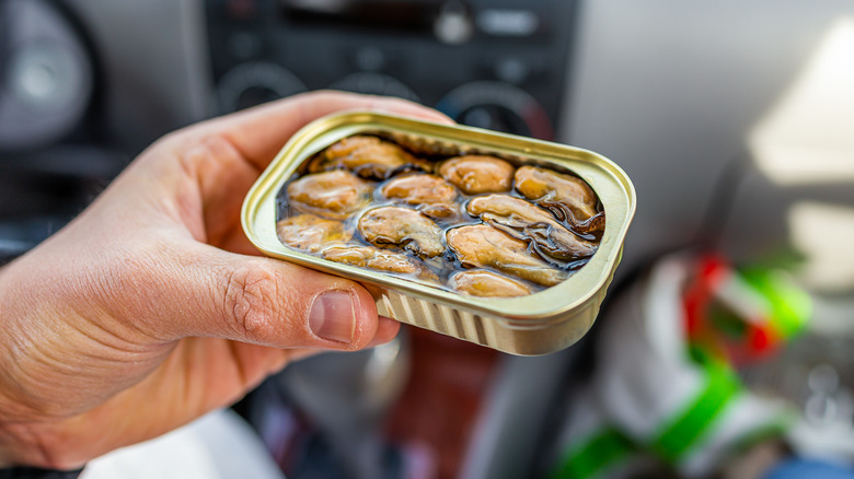 Hand holding an open can of oysters