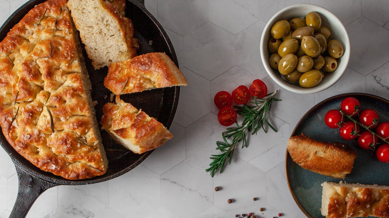 Focaccia in a cast iron skillet served with olives and tomatoes