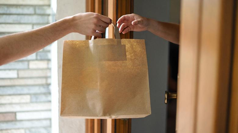 a person handing a bag of food to someone at their doorway