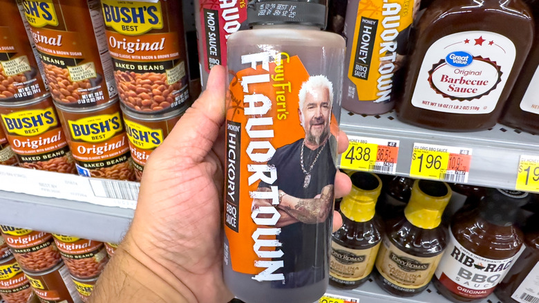 A person holding a bottle of Flavortown BBQ Sauce at store.