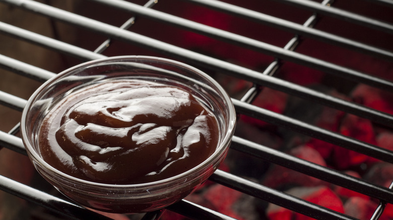 A bowl of barbecue sauce sits on a grill.