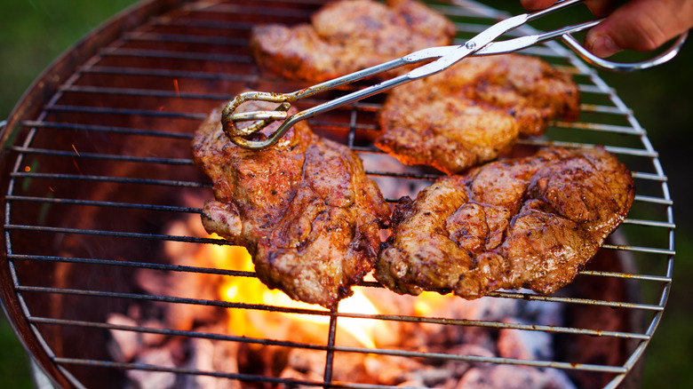 Tongs flip steaks on charcoal grill