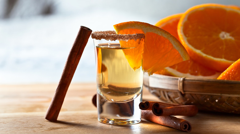 Shot of tequila with spiced rim, cinnamon sticks, sliced oranges, and an orange wedge garnish