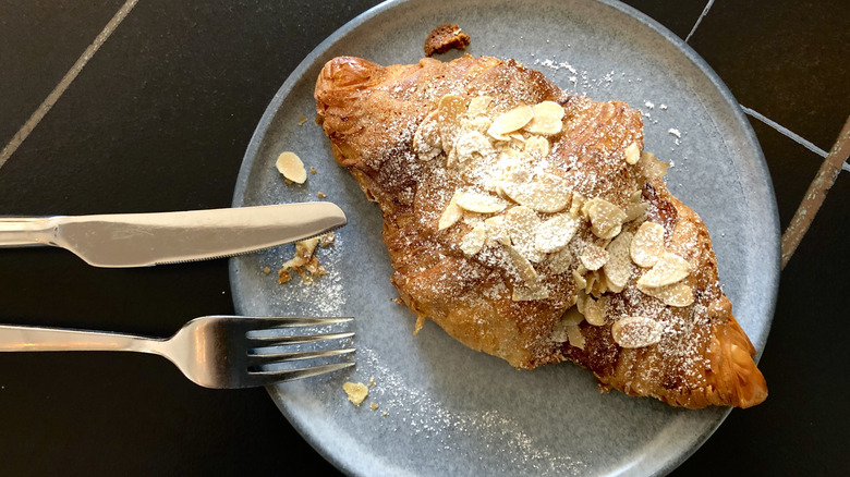 Almond croissant on a plate with a fork and knife