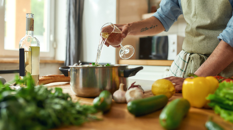 A home cook adding a glass of white wine to a cooking pot
