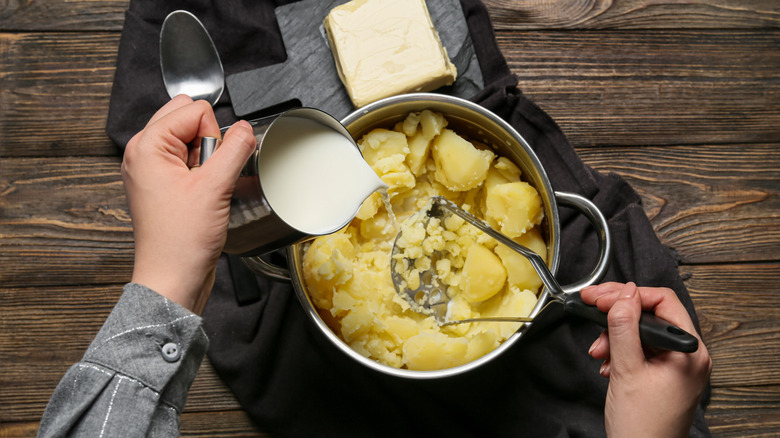 Someone making mashed potatoes by pouring milk into a pot