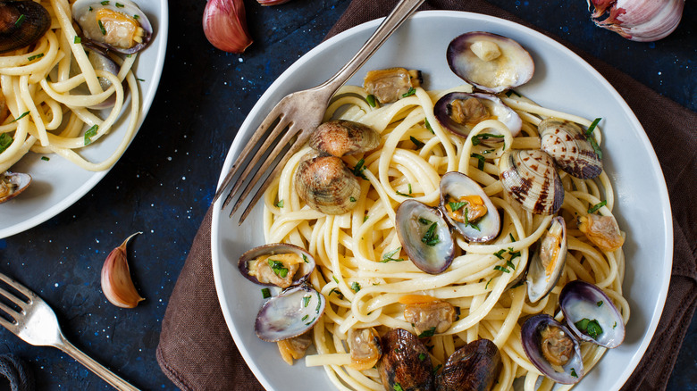 A plate of linguine and clams with garlic cloves around it