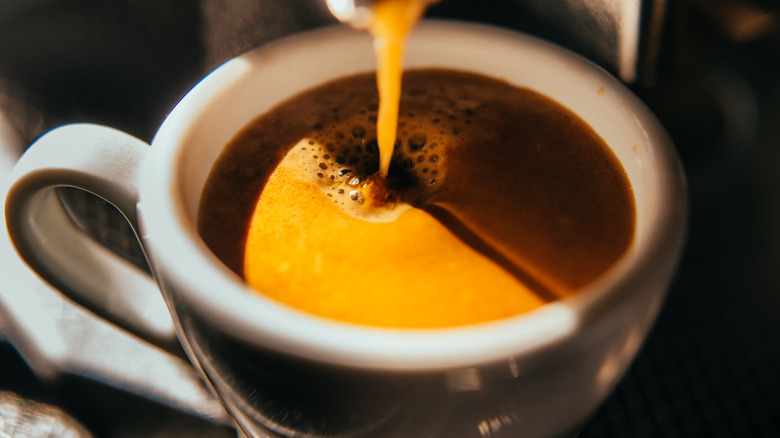 Machine pouring espresso into white cup