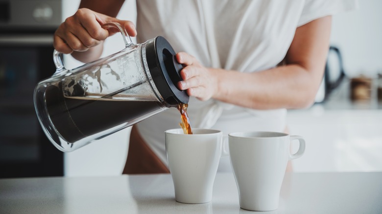 Person pouring two cups of coffee from a French press