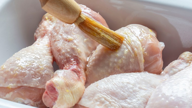 Brushing raw chicken drumsticks with glaze