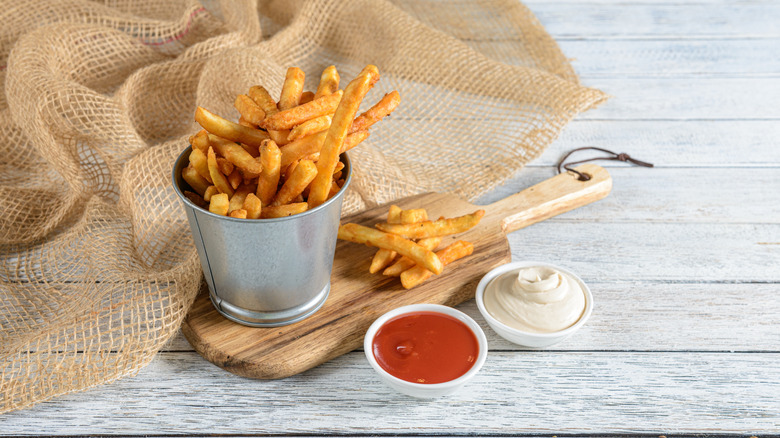 Crispy fries on cup with sauces on wooden paddle and fabric